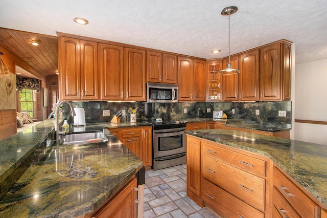 14965 Loon Lake Dr, Bellevue, MI 49021 - kitchen with appliances with stainless steel finishes, a sink, brown cabinetry, pendant lighting, and light stone finish flooring
