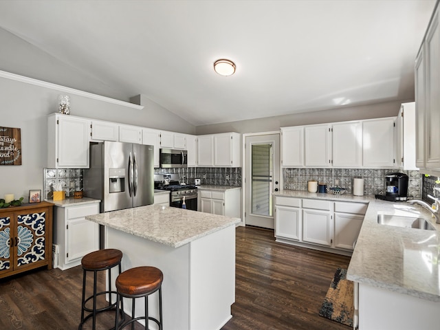 kitchen with stainless steel appliances, a sink, vaulted ceiling, decorative backsplash, and white cabinetry