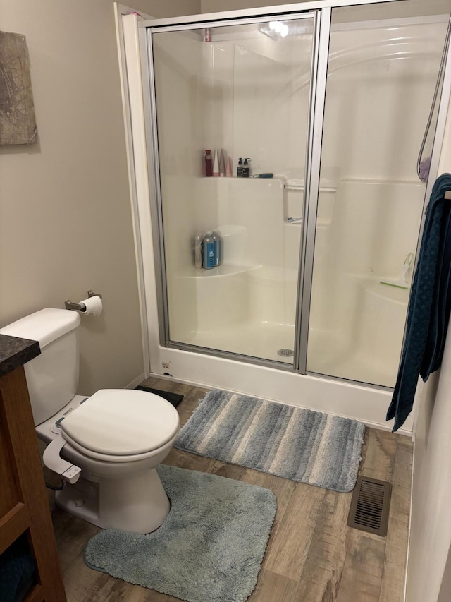 bathroom with wood finished floors, toilet, and a shower stall