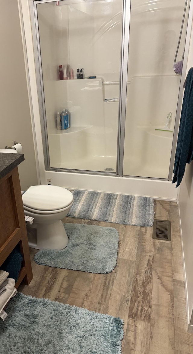 bathroom featuring a shower with shower door, wood finished floors, toilet, and vanity