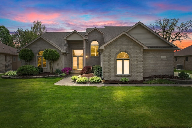 view of front facade with brick siding, a front yard, cooling unit, and a shingled roof