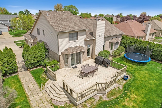 back of house with a deck, a trampoline, a lawn, outdoor dining area, and a gate