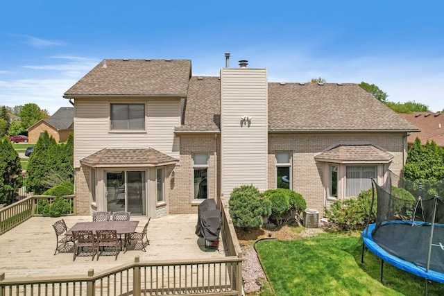 back of house featuring a trampoline, a lawn, brick siding, a shingled roof, and outdoor dining space