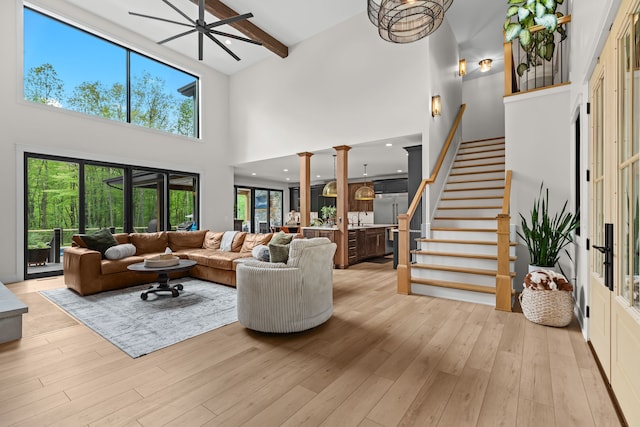 living room featuring a high ceiling, light wood-style floors, stairs, beamed ceiling, and a ceiling fan