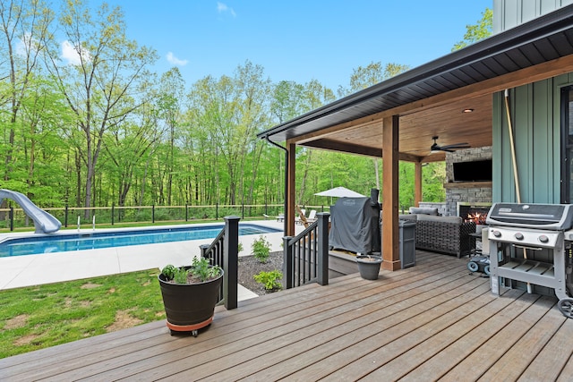 wooden terrace with an outdoor living space with a fireplace, ceiling fan, grilling area, and an outdoor pool