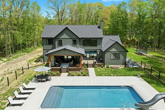 back of house featuring a wooden deck, board and batten siding, a patio area, a shingled roof, and a trampoline