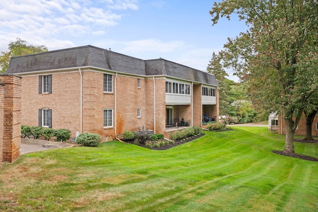 rear view of property with mansard roof, brick siding, a yard, a shingled roof, and a patio area