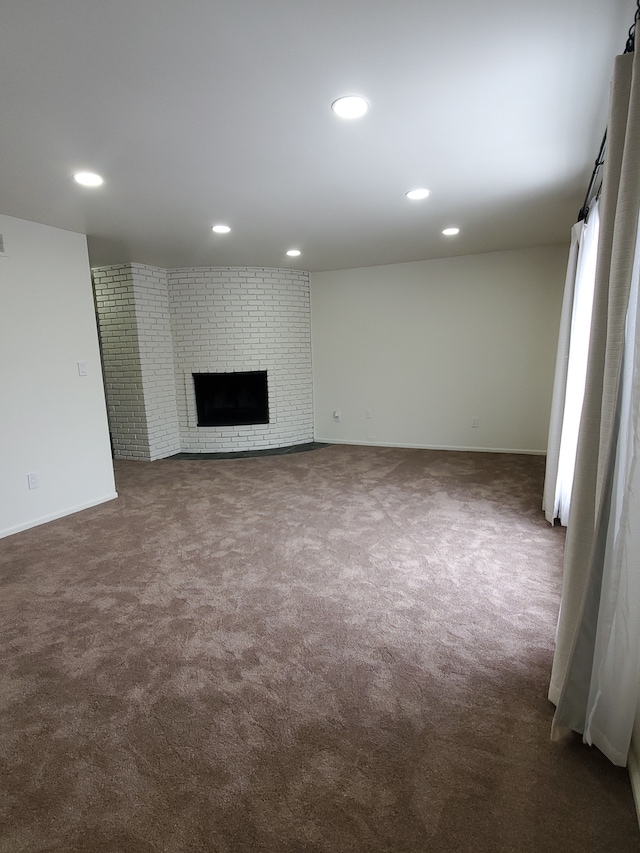unfurnished living room with dark carpet, recessed lighting, a brick fireplace, and baseboards