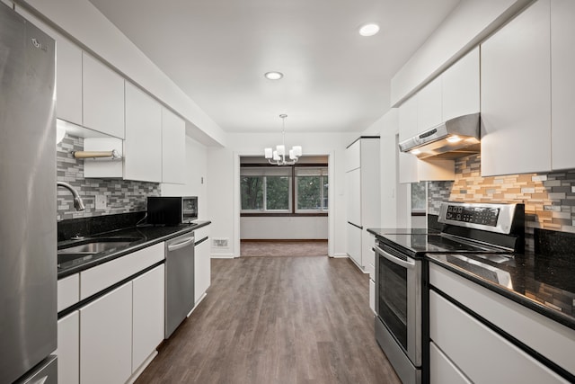 kitchen featuring stainless steel appliances, under cabinet range hood, a chandelier, a sink, and white cabinetry