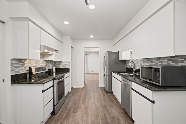 kitchen featuring appliances with stainless steel finishes, a sink, under cabinet range hood, white cabinets, and wood finished floors