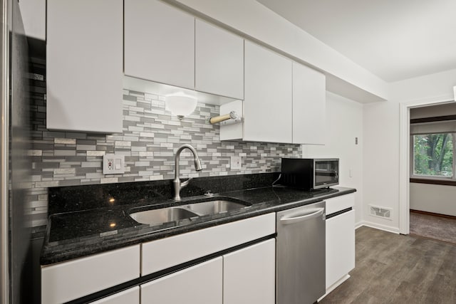 kitchen featuring dishwasher, a sink, white cabinetry, tasteful backsplash, and dark stone counters