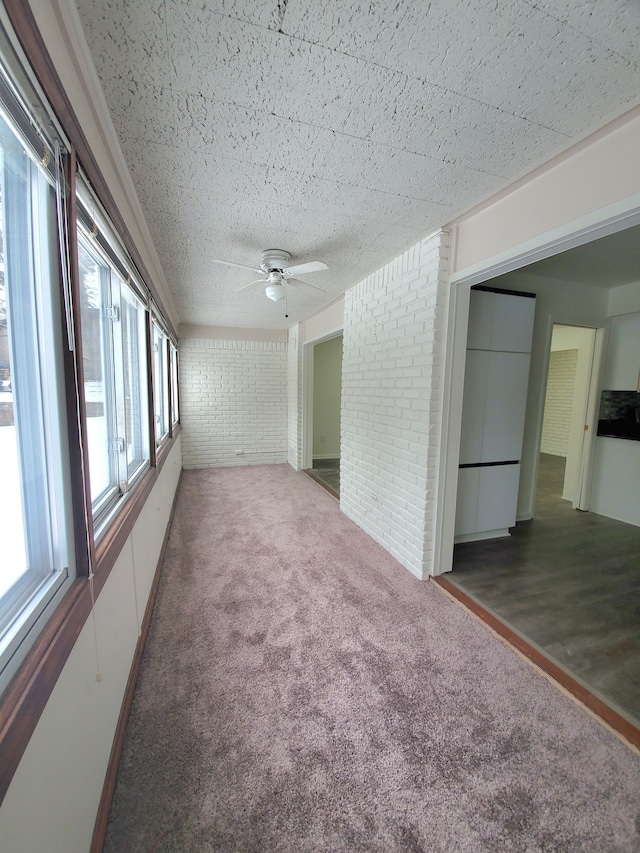 carpeted spare room featuring brick wall and ceiling fan