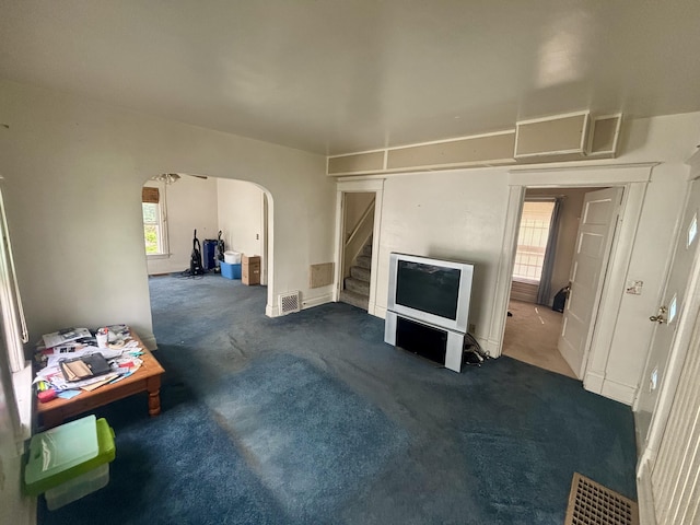 unfurnished living room featuring arched walkways, carpet floors, stairs, and baseboards