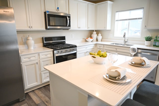 kitchen featuring appliances with stainless steel finishes, a sink, dark wood-style floors, light countertops, and a breakfast bar area