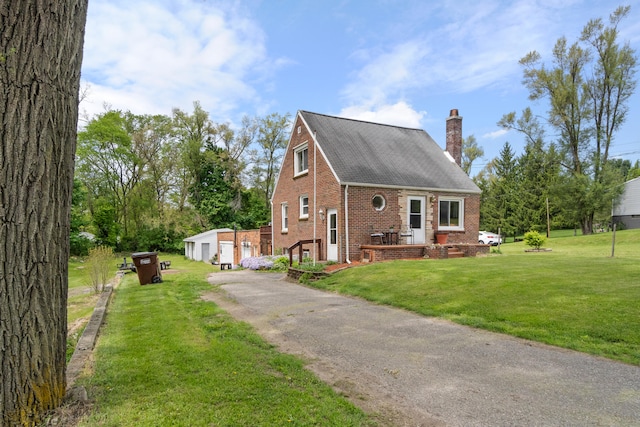 view of front facade featuring brick siding, a chimney, a front yard, roof with shingles, and an outdoor structure