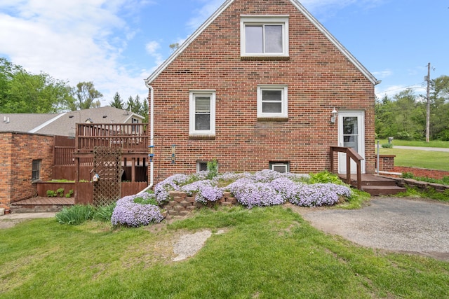 view of side of property with a lawn, brick siding, and a wooden deck