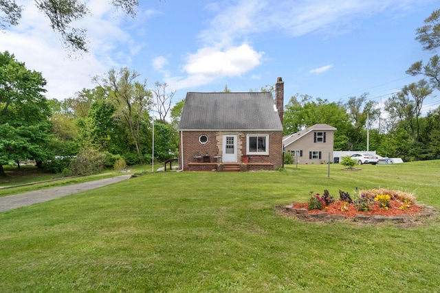 view of front of house featuring a chimney, a front yard, and brick siding