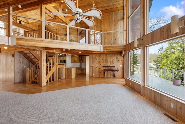 14427 Acorn Cove Trl, Battle Creek, MI 49017 - unfurnished living room featuring high vaulted ceiling, wood walls, carpet floors, a ceiling fan, and stairs