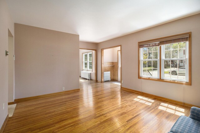 805 E Filer St, Ludington, MI 49431 - unfurnished living room featuring radiator heating unit, radiator, light wood-style flooring, and baseboards