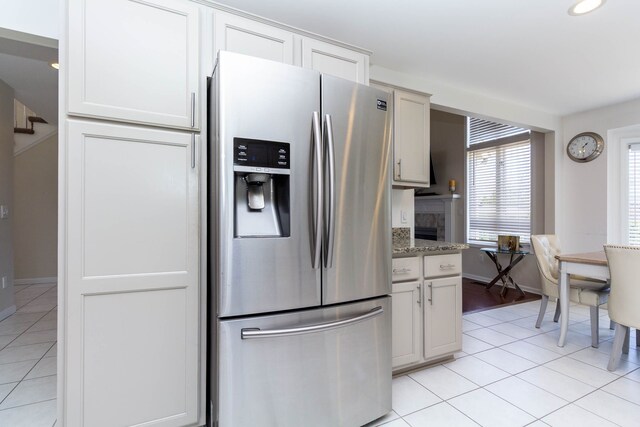 kitchen with stainless steel refrigerator with ice dispenser, light tile patterned floors, baseboards, white cabinetry, and recessed lighting