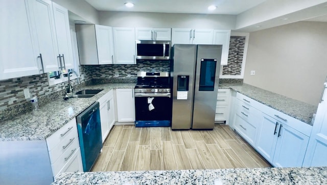 kitchen featuring stainless steel appliances, a sink, white cabinets, recessed lighting, and light stone countertops