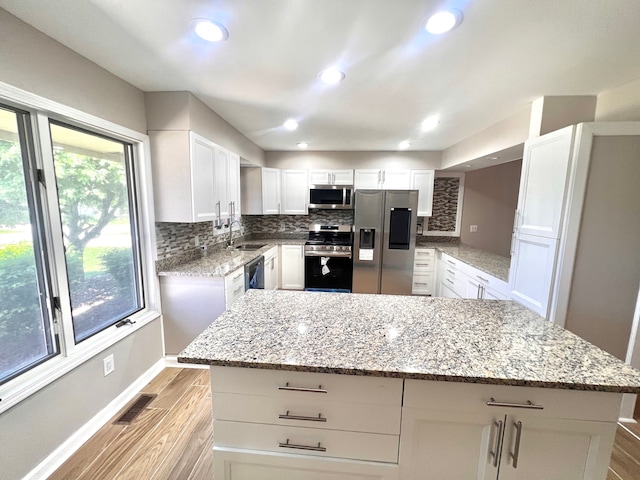 kitchen with stainless steel appliances, a sink, light wood-type flooring, backsplash, and white cabinets