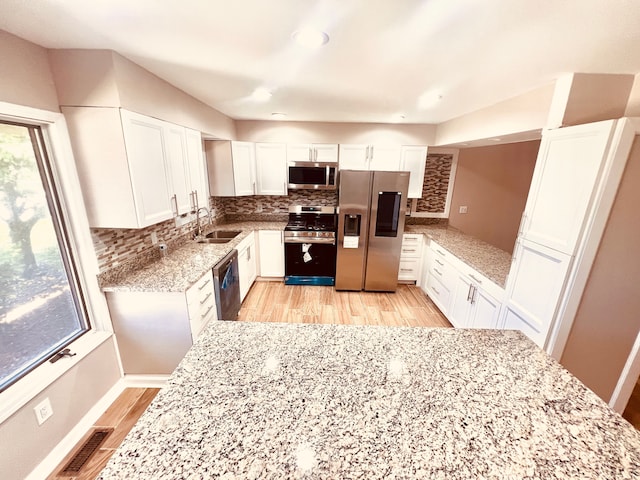 kitchen with stainless steel appliances, a sink, light wood-style flooring, white cabinets, and backsplash