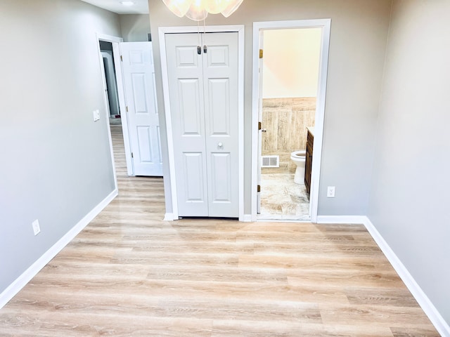unfurnished bedroom featuring light wood-style floors, ensuite bath, a closet, and baseboards