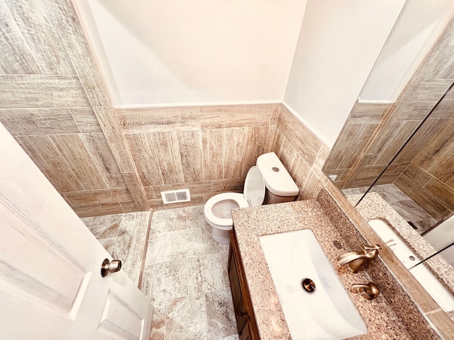 bathroom with toilet, vanity, and a wainscoted wall