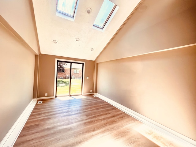 empty room featuring a skylight, baseboards, wood finished floors, and high vaulted ceiling