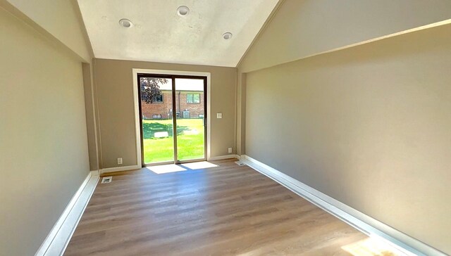 empty room featuring lofted ceiling, wood finished floors, and baseboards