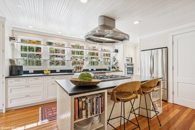 kitchen featuring open shelves, stainless steel appliances, dark countertops, island range hood, and a kitchen bar