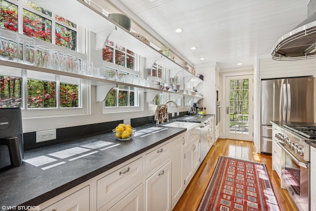 kitchen featuring appliances with stainless steel finishes, open shelves, light wood-type flooring, dark countertops, and white cabinetry