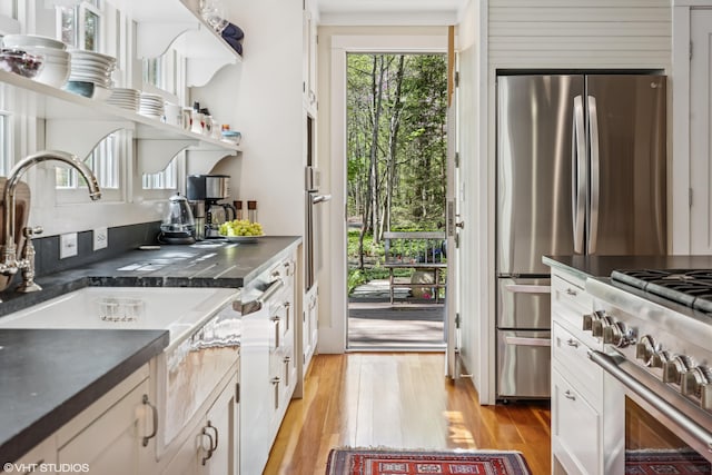 kitchen with dark countertops, light wood-style flooring, a sink, stainless steel appliances, and white cabinetry