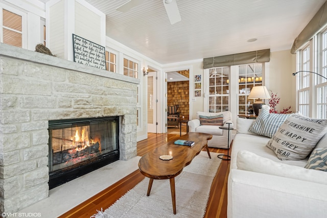 living area featuring a stone fireplace, wood finished floors, and a ceiling fan