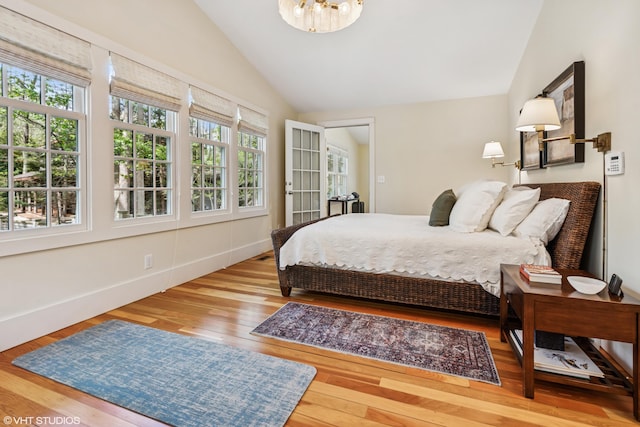 bedroom featuring vaulted ceiling, multiple windows, wood finished floors, a chandelier, and baseboards