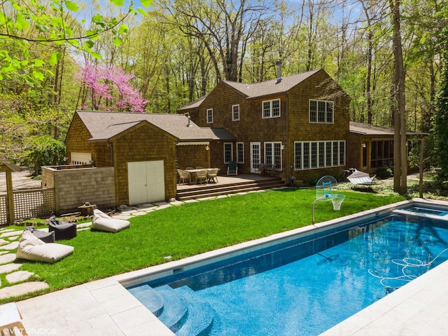 back of house featuring a yard, a wooden deck, a pool with connected hot tub, a garage, and a shingled roof
