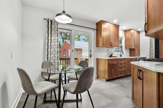 kitchen with light countertops, decorative backsplash, brown cabinetry, recessed lighting, and decorative light fixtures