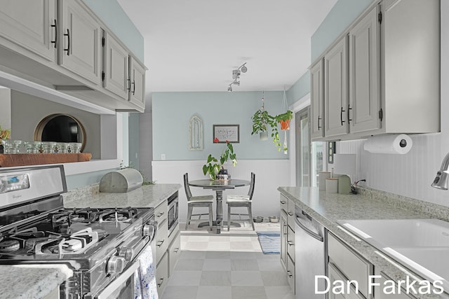 kitchen with appliances with stainless steel finishes, a sink, light countertops, a wainscoted wall, and tile patterned floors