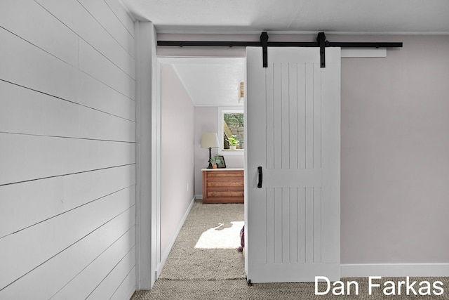 hallway with a barn door, carpet flooring, and baseboards