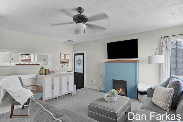 living room with ceiling fan, light colored carpet, a tile fireplace, baseboards, and a textured ceiling