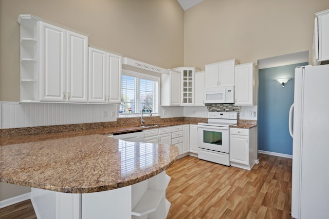 kitchen featuring open shelves, white appliances, high vaulted ceiling, a sink, and a peninsula