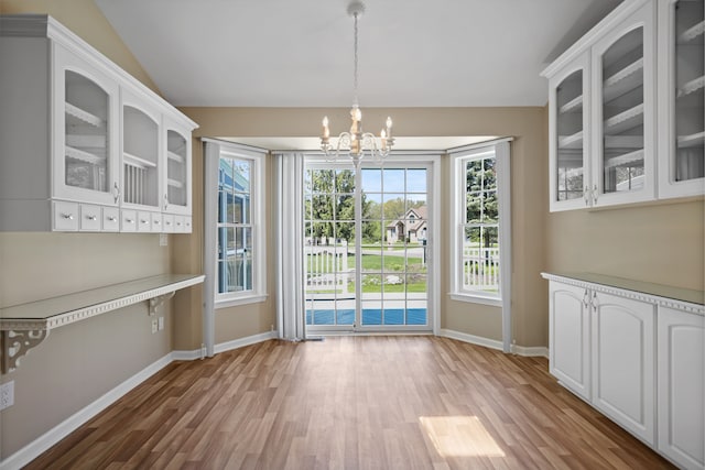 unfurnished dining area with a chandelier, light wood-style floors, baseboards, and lofted ceiling