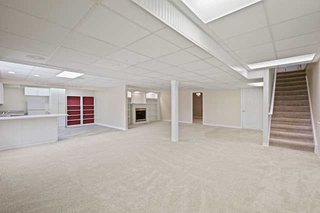 finished basement with freestanding refrigerator, light carpet, a paneled ceiling, a fireplace, and stairs