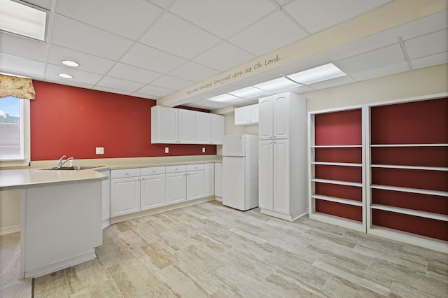 kitchen with freestanding refrigerator, a drop ceiling, light countertops, white cabinetry, and a sink