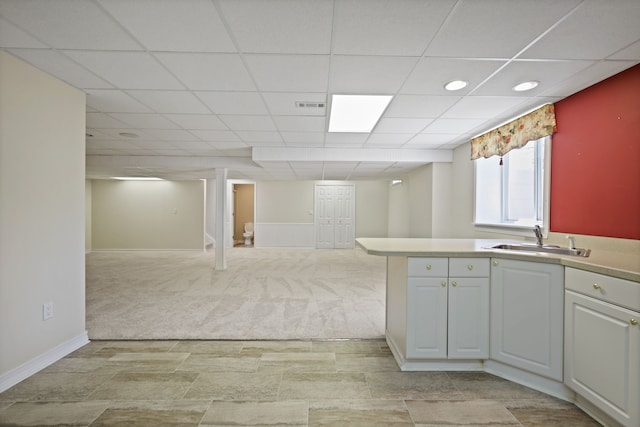 kitchen featuring a sink, baseboards, a drop ceiling, light countertops, and light colored carpet
