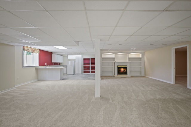 basement with freestanding refrigerator, light carpet, baseboards, and a drop ceiling