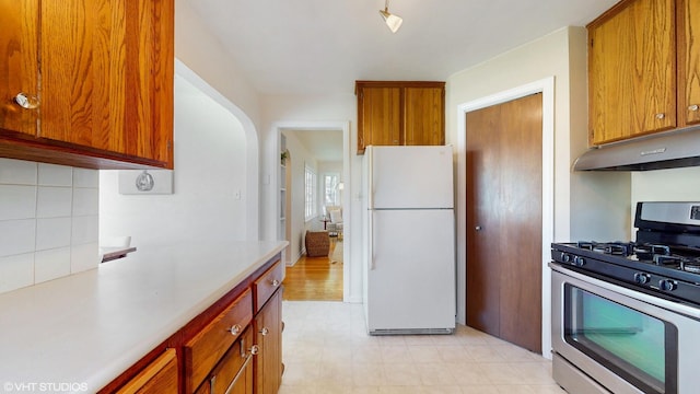 1200 Mohawk Ln, Saint Joseph, MI 49085 - kitchen featuring freestanding refrigerator, gas range, under cabinet range hood, light countertops, and brown cabinetry