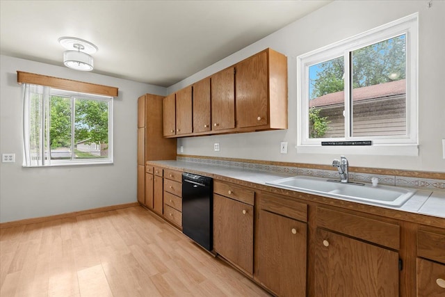 kitchen featuring dishwasher, a sink, brown cabinetry, light wood-style floors, and light countertops