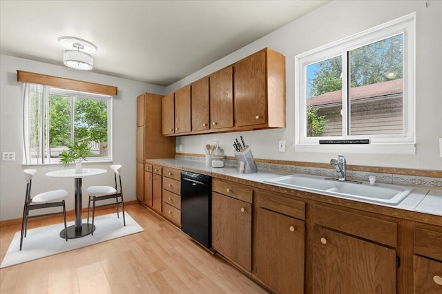 kitchen with dishwasher, a sink, light wood-style flooring, brown cabinetry, and light countertops
